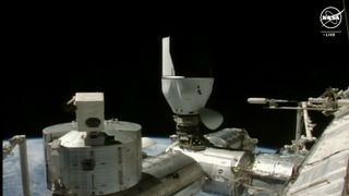 a spacecraft capsule is docked upside down to the upward docking port of a chrome space station module.