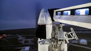 A black and white spacecraft on a white rocket at its launch pad with an access arm